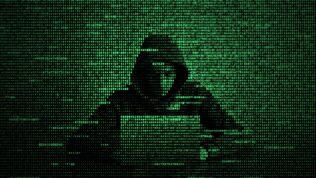 A hacker typing on a keyboard behind a screen of computer code